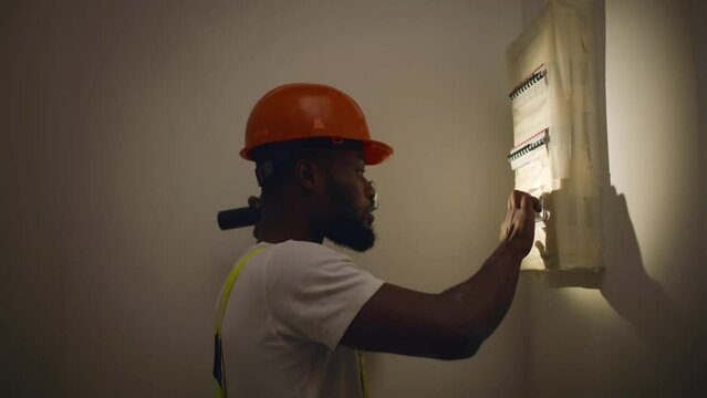 African-American builder with flashlight check switches on fuse block. Realtime