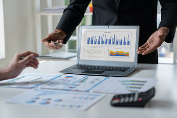 A group of Asian businessmen are brainstorming to analyze financial reporting situations. Calculate investments with income, tax and accounting calculators from graphs data on laptop at desk.