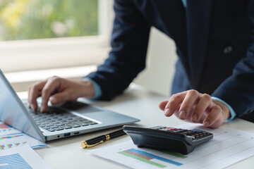 Young businessman analyzing Calculate with investment calculator, income, tax, account from data graph. Financial income in real estate projects View earnings on laptop at office desk.