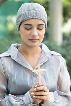 Happy smiling south asian Indian woman cancer patient wearing head scarf praying for god with holy cross, concept image of strong religion faith and sickness