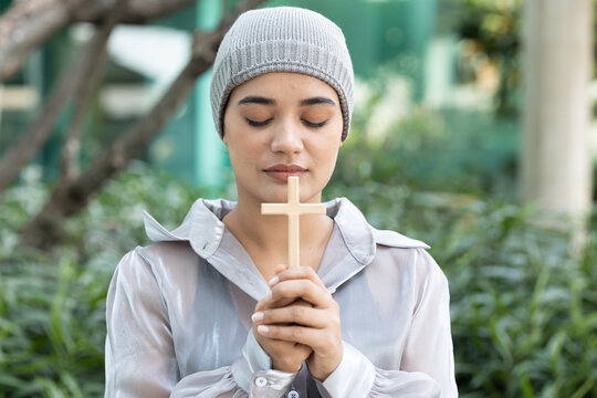 Happy smiling south asian Indian woman cancer patient wearing head scarf praying for god with holy cross, concept image of strong religion faith and sickness