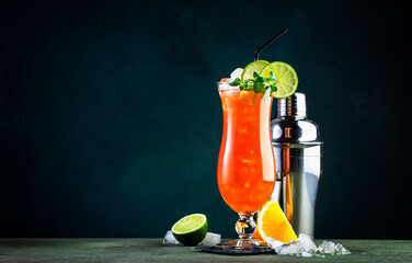 Hurricane alcoholic cocktail with dark and white rum, ice, grenadine, pineapple and orange juice, lime and ice, garnished with mint. Dark background, bar tools