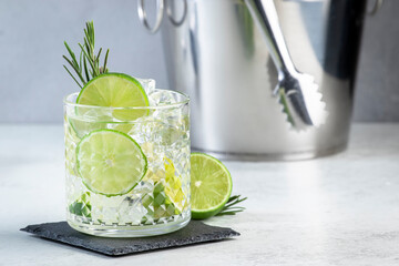 Gin tonic classic cocktail drink with dry gin, bitter tonic, lime and ice. Gray table background