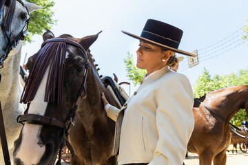 Obraz premium Young woman dressed in traditional flamenco custom and hat stroking her horse at the seville fair