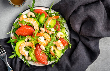 Seafood salad with shrimps, avocado, grapefruit, arugula and cashews. Gray stone kitchen  table background, top view