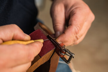 Obraz na płótnie Canvas Man making holes in leather belt with stitching awl