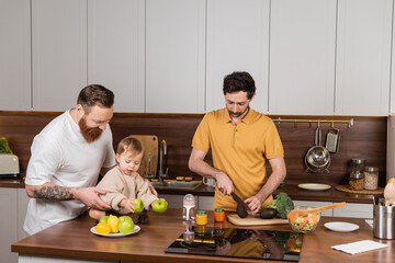 Fototapeta na wymiar Gay man cooking near partner and toddler daughter in kitchen.