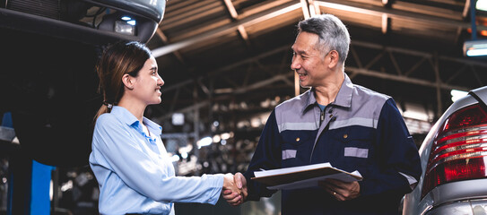 Young female car service manager giving quotation on a clipboard to senior male client and customer...