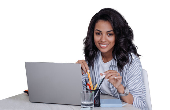 Cute toothy smiles African American young woman in casual sitting at desk with laptop looks at camera, works home. Cheerful Brazilian girl ready for distant lesson against transparent background