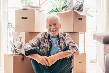 Happy senior man sitting on floor relaxing in new home living room with cardboard boxes packed with...