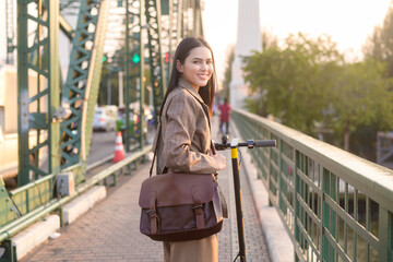 Portrait of young business woman with an electric scooter to work over bridge in modern city  background