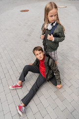 overhead view of preteen boy in trendy bomber jacket sitting on penny board near girl in wireless...