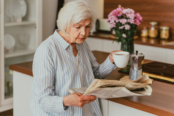 Elderly woman having breakfast and reading newspaper at home