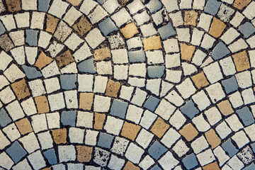 Vintage mosaic flooring fragment. Small squares in white, blue and yellow stone with black grout.