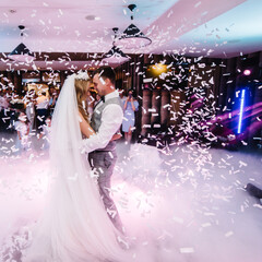 First wedding dance of newlywed. Happy bride and groom dancing under confetti in the elegant...
