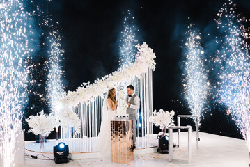 Bride and a groom is cutting and eating wedding cake. Hands cut the cake with flowers. Newlywed...