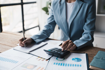 Close up view of young Asian businesswoman using calculator while analyzing the project budget in office desk.