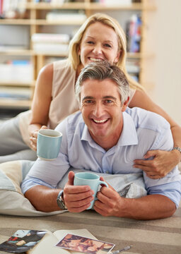 Love and laugh together. Portrait of a mature couple lying on the floor drinking coffee and looking at photographs.