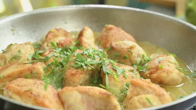 The chef sprinkles fresh tarragon over the chicken pieces in a frying pan.
