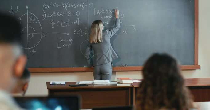 Caucasian female professor at high school writing on blackboard while explaining math for students. University knowledge. Woman teacher explaining mathematics formulas and teaching.