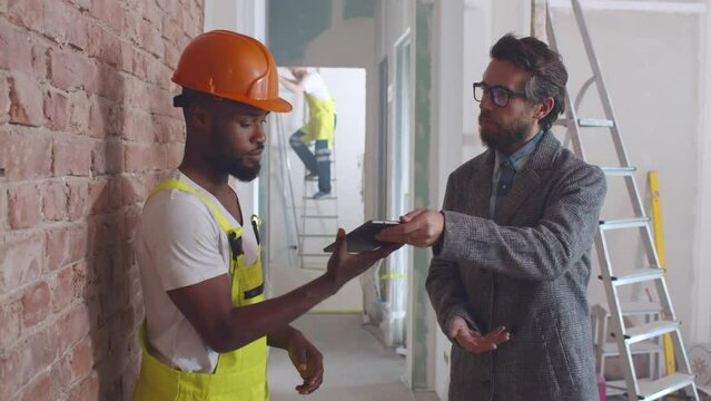 Businessman sign document on tablet and shake hands with foreman on construction site. Realtime