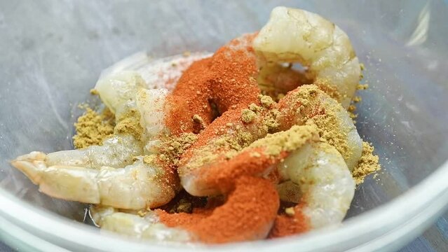 The chef sprinkles cumin over the shrimp in a glass bowl.
