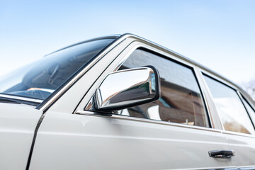 Low angle view of a chrome side mirror of a white car against a blue sky