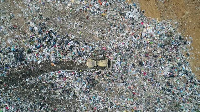 Aerial top down view of the bulldozer moves along the landfill, leveling the garbage. gulls feeding on food waste fly over It. Waste conservation. Trash disposal on rubbish dump