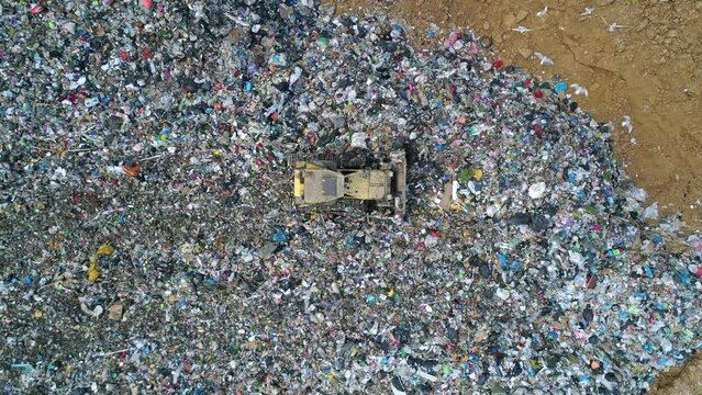 Aerial top down view of the bulldozer moves along the landfill, leveling the garbage. gulls feeding on food waste fly over It. Waste conservation. Trash disposal on rubbish dump