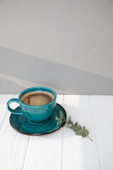 Blue mug with coffee, cappuccino, tea on a white wooden table with shadows. Top view, close-up