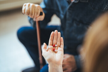Obraz premium A young nurse sits at a table in the living room with a senior man and provides him with medical assistance. Female Doctor giving medication to elderly patient sitting on sofa
