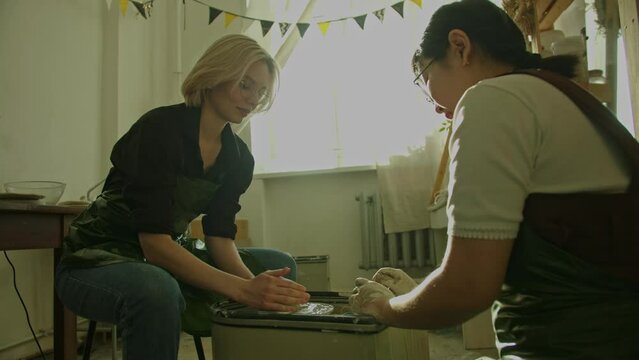 Girl teaching woman in her atmospheric craft workshop pottery studio