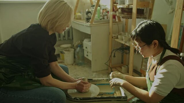 Girl teaching woman in her atmospheric craft workshop pottery studio