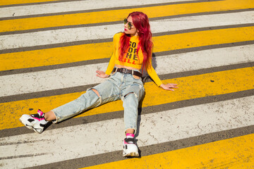 A lady with pink hair in sunglasses, a yellow top and ripped jeans sits on the sidewalk. Vintage retro style clothing from the 2000s in modern fashion. The return of old trends in a new way