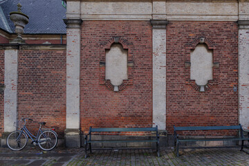 Front parallel outdoor view of old black bench and bicycle lean in front of exterior old rough brick wall in Copenhagen, Denmark.