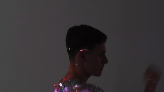 Lgbtq party. Male dancer. Double exposure magic. Tranquil man in spangle shirt rainbow color earrings moving on gray with galaxy purple blue sparkle lights overlay background.