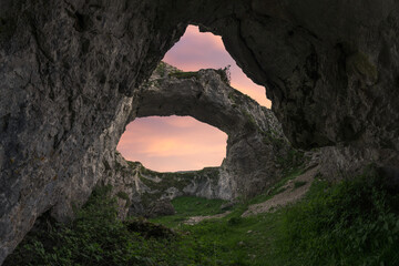 Double hole cave in mountainous terrain against sunset sky