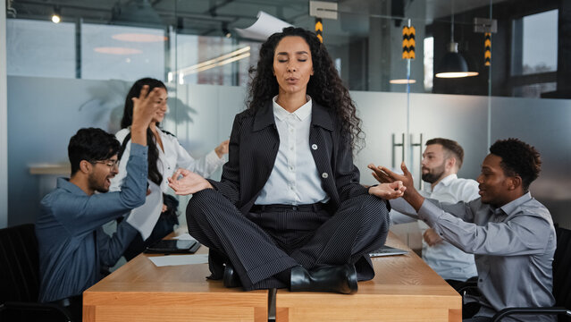 Calm businesswoman professional taking break meditating sitting at table in office meeting ignoring loud colleagues discussing brainstorming argue mindful healthy female boss doing yoga no stress zen