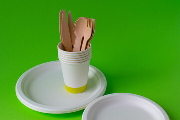 Eco-friendly disposable dishes made of bamboo wood and paper on a green background. Draped spoons,...