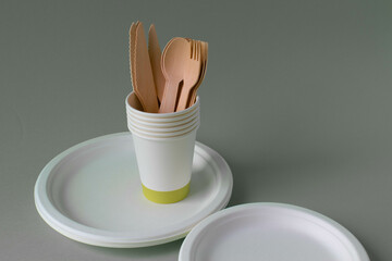 Eco-friendly disposable dishes made of bamboo wood and paper in the background. Draped spoons, forks, knives, bamboo plates with paper cups