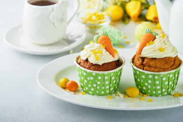 Carrot cake cupcakes for Easter. Carrot cupcakes with cream cheese frosting decorated with tiny marzipan carrots on white background. Happy Easter and spring holiday concept. Holydays homemade dessert
