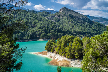 Lake Guadalest, rocky mountains and hills covered with trees. Blue sky