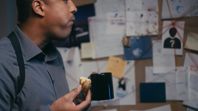 Busy investigator having lunch at work, eating donut near evidence board on wall