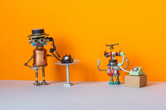 Two toy operator robots are holding vintage telephone handsets. The concept of a customer service phone hotline using robots and artificial intelligence