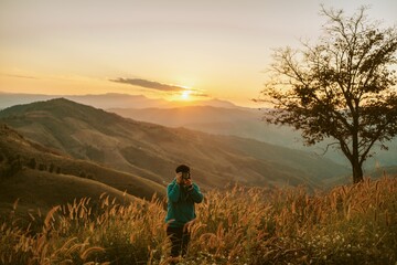 Travel tourist alone Hiking adventure. Young man standing on top of cliff in summer mountains with sunset enjoy view nature cliff mountain