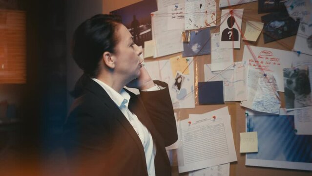 Busy female detective talking on phone, crime evidence board in police office