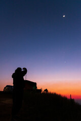 Women taking picture of nature observing evening sky with stars, planets and crescent moon. Moon meets Jupiter and Venus in the twilight sky. © pjjaruwan