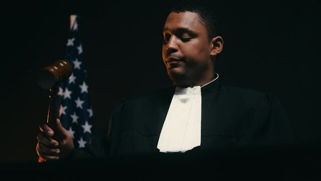 Male judge striking gavel, calling to order in courtroom, US flag background