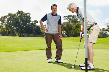 Golfing is a great way to bond. Two men out on the green playing a round of golf together.