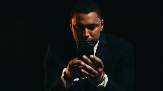 Corrupt male politician in cuffs using smartphone, contacting lawyer to pay bail